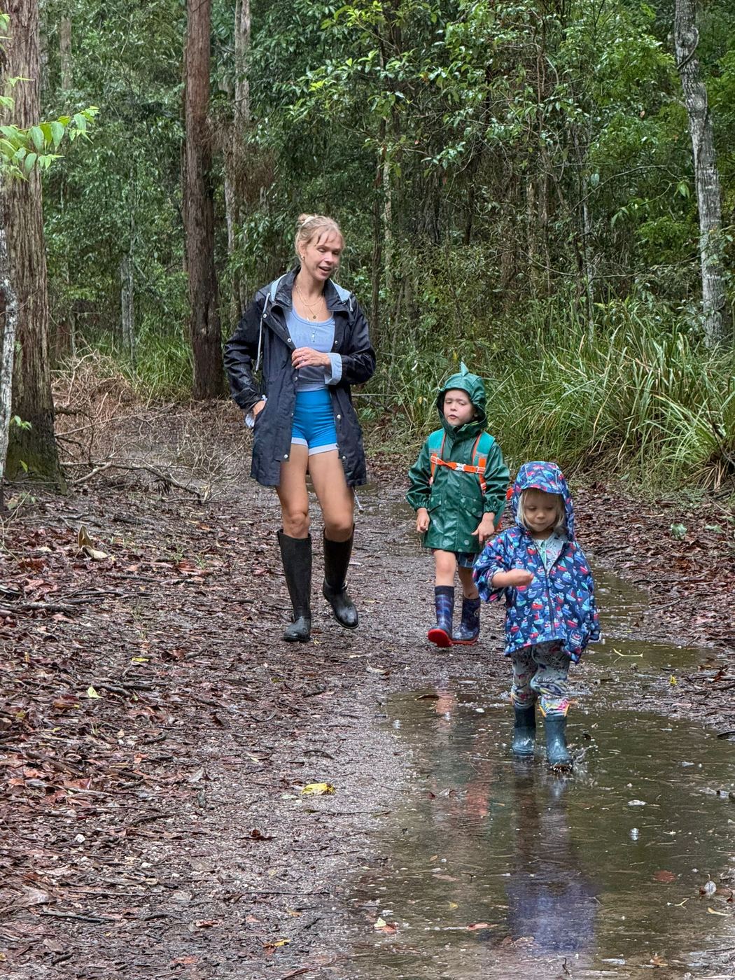 Sally and her two boys in raincoats splashing along a muddy forest trail